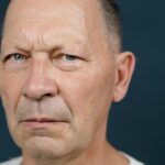 Close-up of a serious senior man with a bald head on a dark background.